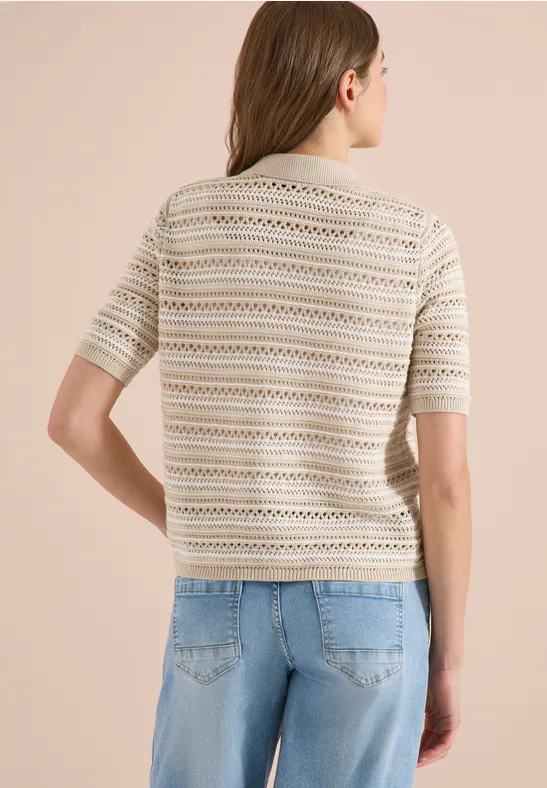 Vue de dos d’une femme portant un pull fin beige à motifs et un jean bleu sur fond clair.