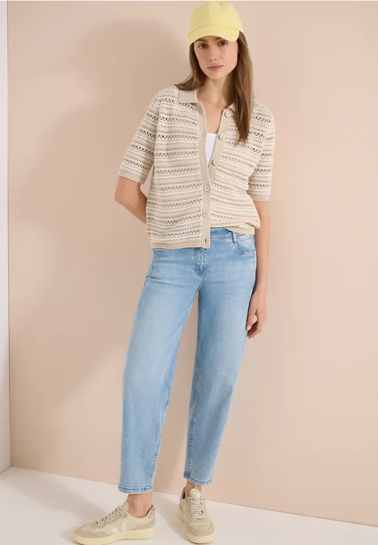 Femme en chemise rayée à manches courtes, top blanc, jean bleu décontracté et baskets sur fond clair.