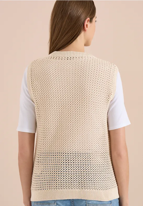Vue de dos d'une femme portant une veste beige crochetée sur un t-shirt blanc.