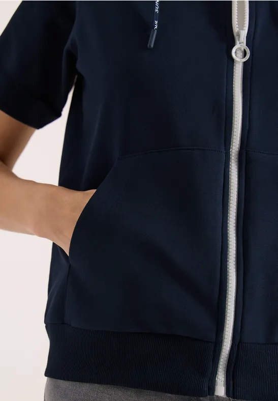 Une personne porte un sweat à capuche bleu marine à fermeture éclair et a la main dans la poche avant.