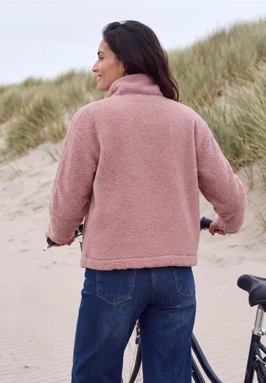 Une femme en polaire rose sur la plage, regard vers la mer, un vélo à côté.