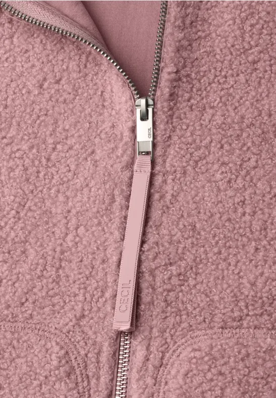 Gros plan d’une veste en polaire peluche rose, fermeture éclair argentée et texture douce et moelleuse.