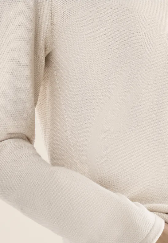 Nahaufnahme eines beige gestrickten Pullovers mit Langarm, zeigt Textur und weiches Material.