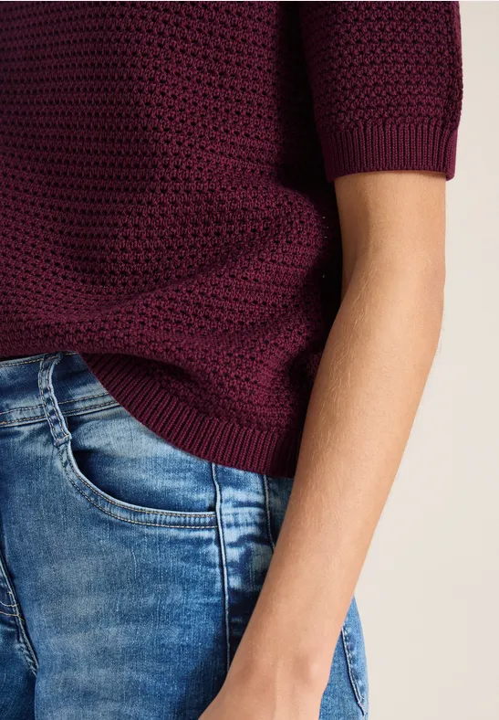 Teilansicht einer Person mit weinrotem Strickoberteil und blauen Jeans