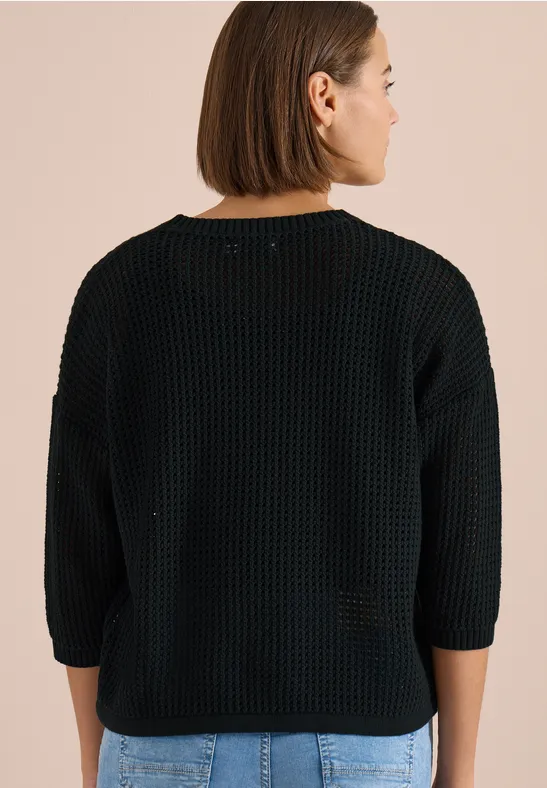 Rückenansicht einer Person in schwarzem grob gestricktem Pullover mit 3/4-Ärmeln vor beigem Hintergrund