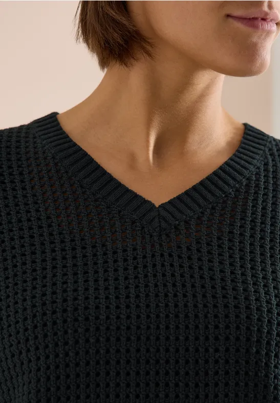 Nahaufnahme eines Oberkörpers in grobem schwarzen Strickpullover mit V-Ausschnitt.