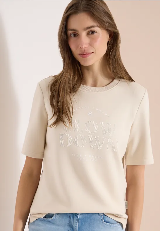 Jeune femme portant un t-shirt beige à manches courtes devant un fond neutre