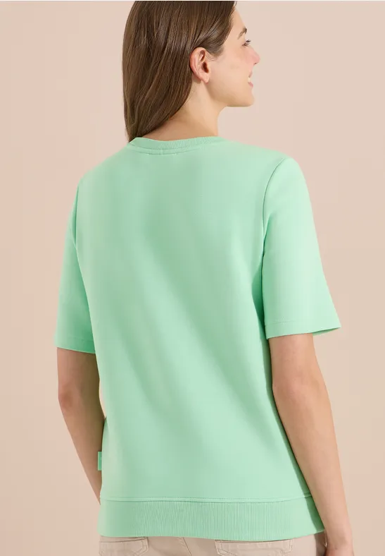 Vue de dos d'une personne portant un t-shirt vert menthe et cheveux mi-longs sur fond clair.