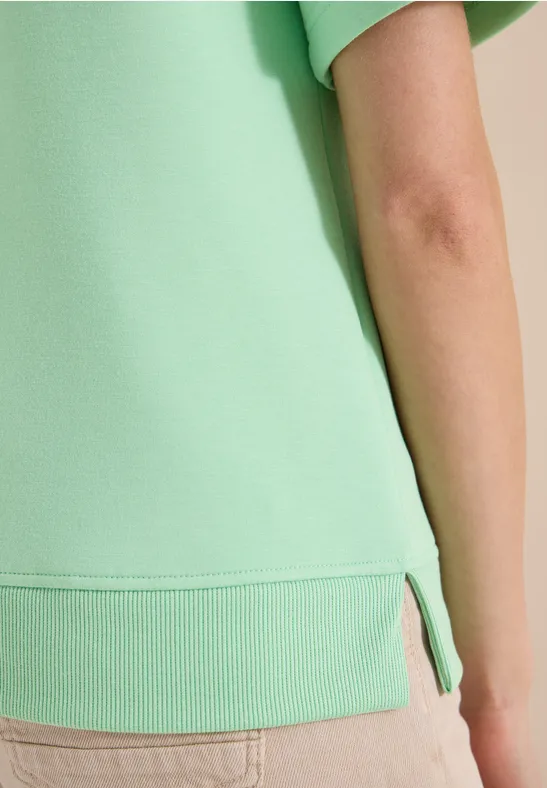 Gros plan d'une personne en t-shirt vert clair, bras droit et fente latérale de l'ourlet visibles