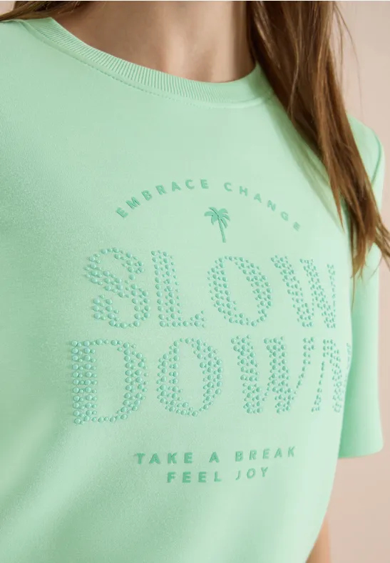 T-shirt vert clair avec inscription en relief "SLOW DOWN" et petit slogan motivant.