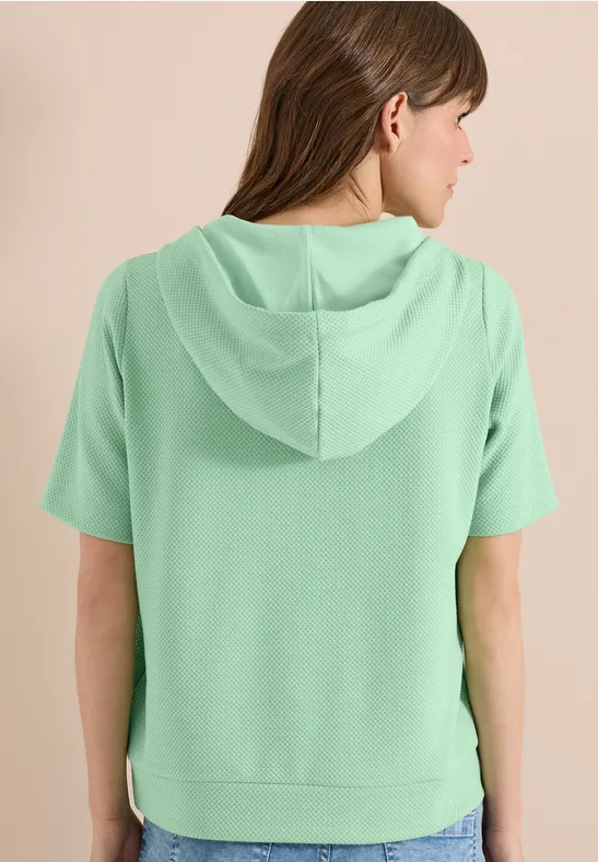 Femme de dos portant un sweat à capuche manches courtes vert menthe.