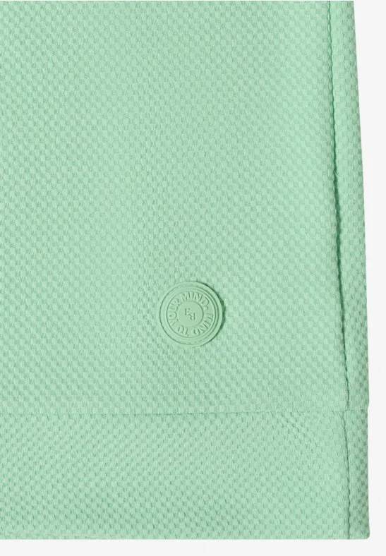 Gros plan sur un tissu vert menthe texturé avec un petit logo circulaire embossé.