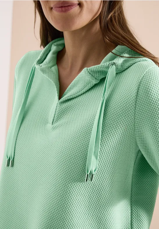Femme portant un sweat à capuche vert menthe texturé avec encolure en V et cordons.