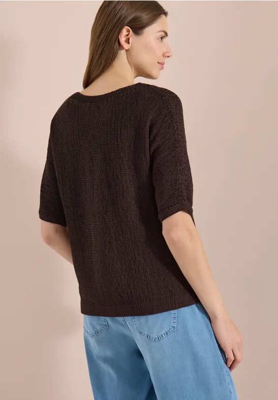 Rückenansicht einer Frau in braunem Strukturstrickshirt mit halblangen Ärmeln und blauen Jeans.