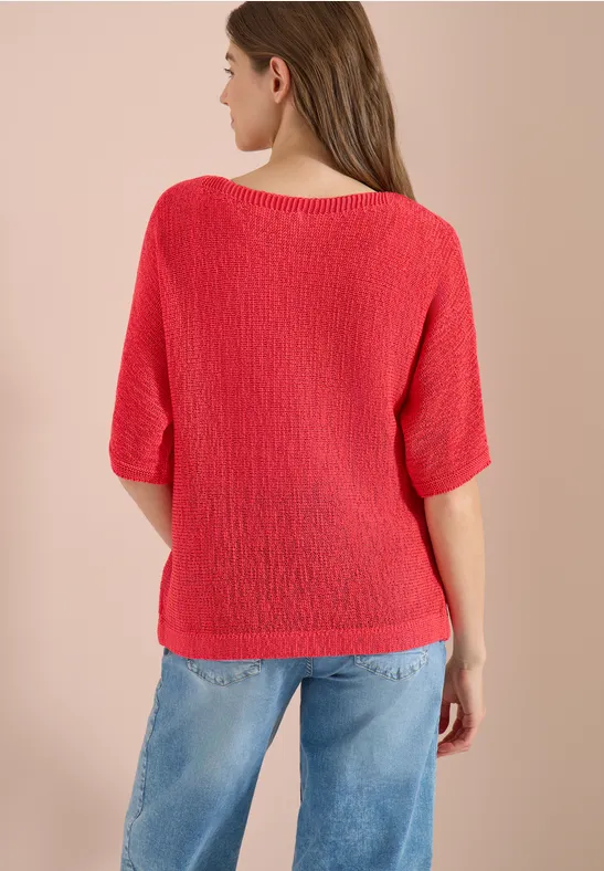 Rückansicht einer Frau in rotem, lockerem Strickpullover mit halblangen Ärmeln und blauen Jeans.