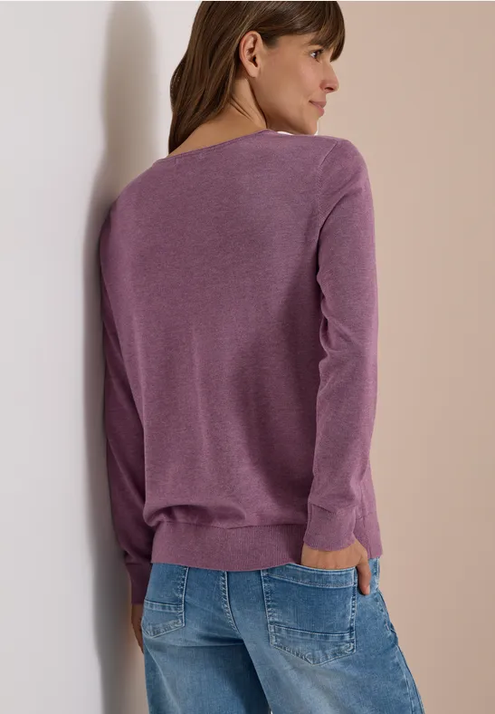 Femme vue de dos portant un pull violet clair et un jean bleu sur un fond neutre.