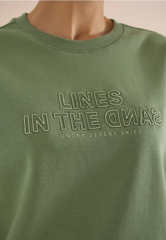 T-shirt vert olive avec l'inscription « LINES IN THE SAND » et « UNDER DESERT SKIES » en lettres imprimées.
