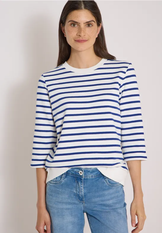 Femme en t-shirt blanc à rayures bleues trois-quarts et jean bleu.