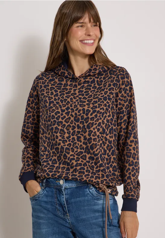 Femme souriante en pull marron à motif léopard, cordon à la taille et jean bleu