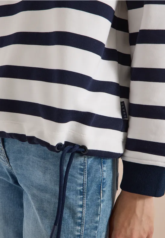 Person trägt blau-weißen Streifenpullover mit Kordelzug und Jeans.