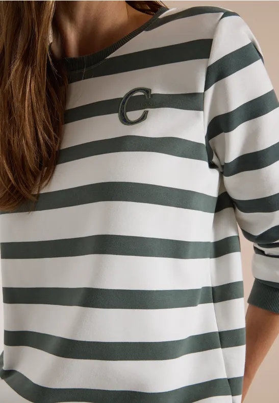 Une personne porte un T-shirt blanc à rayures vertes à manches 3/4, encolure arrondie et petit logo C.