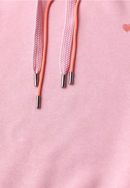 Gros plan d'un sweat rose avec cordons et embouts métalliques argentés.