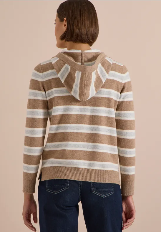 Frau von hinten in gestreiftem Kapuzenpullover in Beige und Weiß, kombiniert mit blauen Jeans.