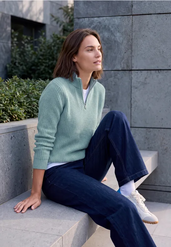 Femme en tenue décontractée assise sur un banc en pierre, regard détendu vers l'horizon.