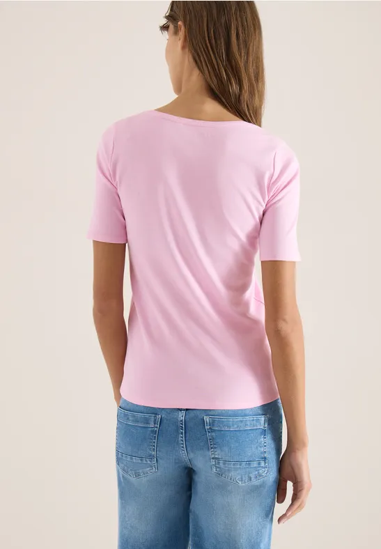 Vue de dos d’une femme portant un t-shirt rose et un jean bleu sur fond clair.