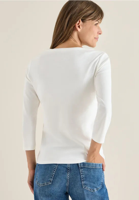 Frau mit weißen Langarmshirt und Jeans von hinten.