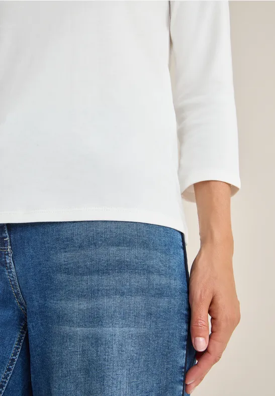 Person mit weißem Shirt und blauer Jeans, Hand seitlich sichtbar.
