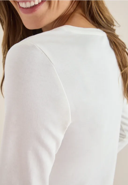 Eine Frau lächelt und trägt ein weißes Langarmshirt.