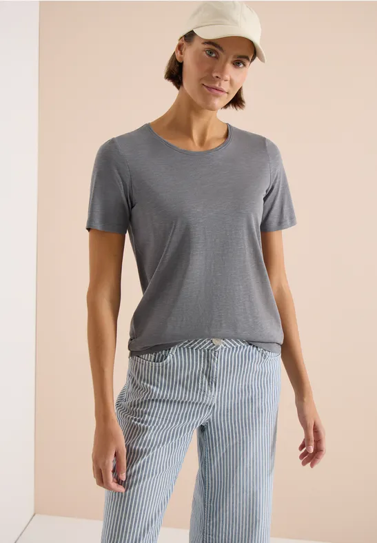 Eine Person trägt ein schlichtes graues T-Shirt und blau-weiß gestreifte Hosen.