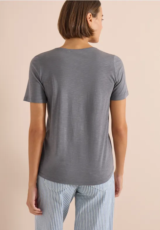 Person von hinten in grauem T-Shirt und hellblauer, gestreifter Hose vor beigem Hintergrund.