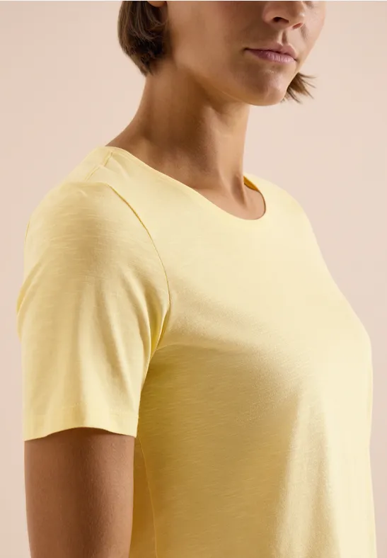 Nahaufnahme einer Person mit hellem gelbem T-Shirt, kurzen Ärmeln und Rundhalsausschnitt.