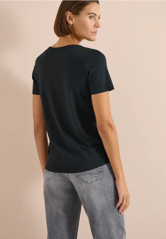 Frau von hinten in schwarzem T-Shirt und grauen Jeans vor beigem Hintergrund.