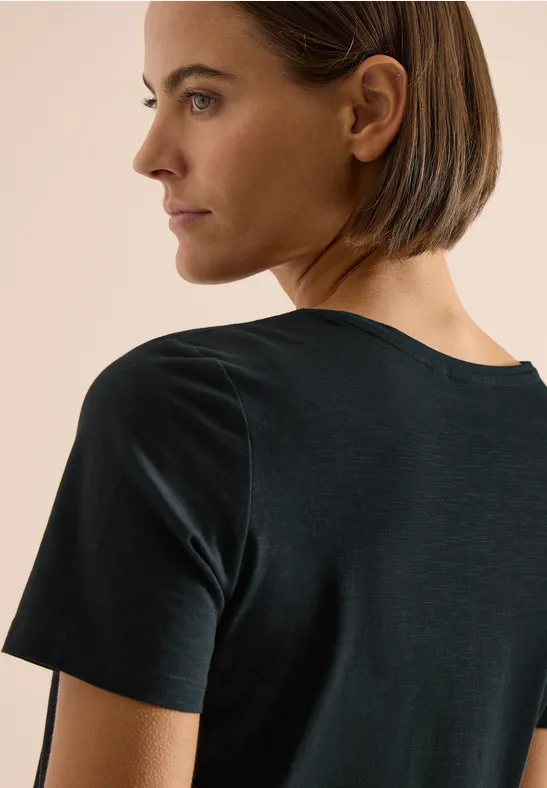 Seitenansicht einer Person mit kurzem braunem Haar in einem schwarzen T-Shirt vor hellem Hintergrund.