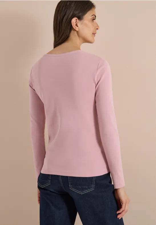 Femme de dos portant un t-shirt à manches longues rose et un jean bleu sur fond clair