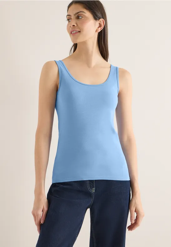 Frau trägt ein hellblaues Top und dunkle Jeans.