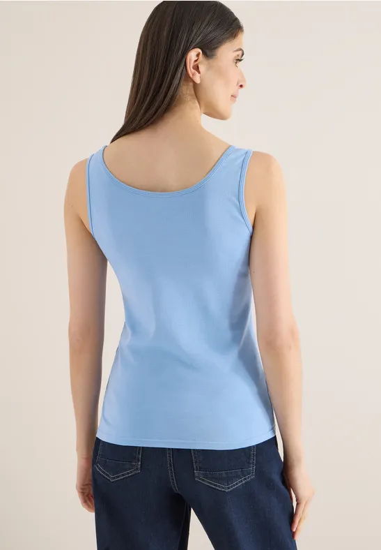 Eine Frau von hinten in einem hellblauen ärmellosen Top und dunkler Jeans.