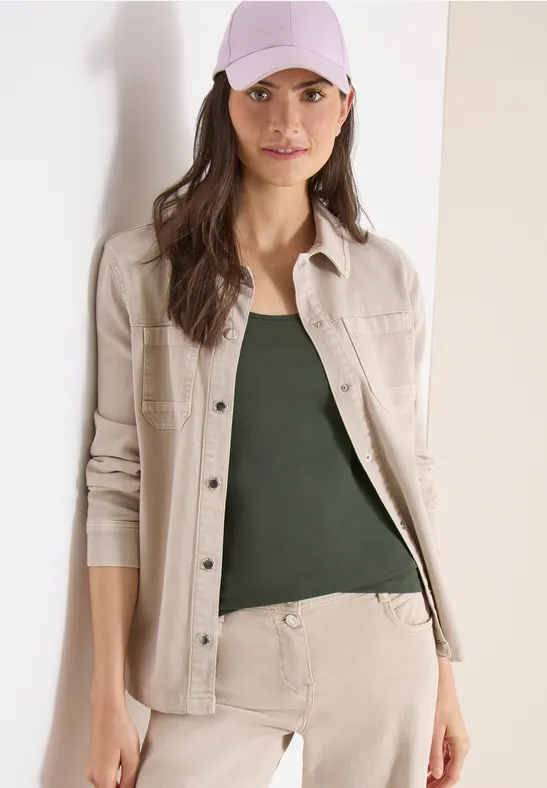 Frau trägt beige Hemdjacke, olivgrünes Top und beige Hose.