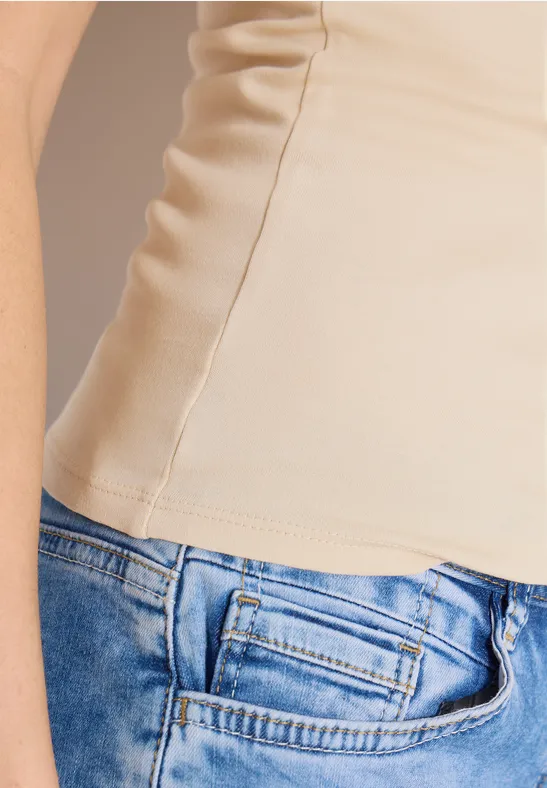 Seitansicht eines Oberkörpers mit beigem Top und blauen Jeans.