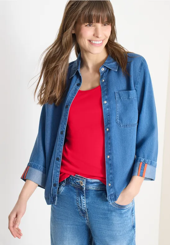 Person trägt blaues Jeanshemd über rotem Top und blaue Jeanshose.