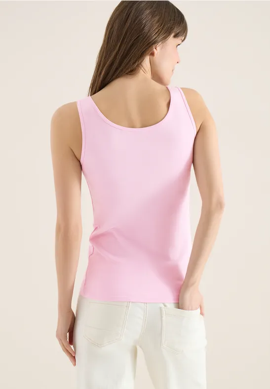 Vue de dos d’une femme portant un débardeur rose et un pantalon blanc sur fond clair.