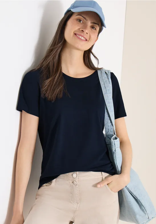 Person in schwarzem Shirt, beiger Hose und blauer Umhängetasche, dazu blaue Mütze.