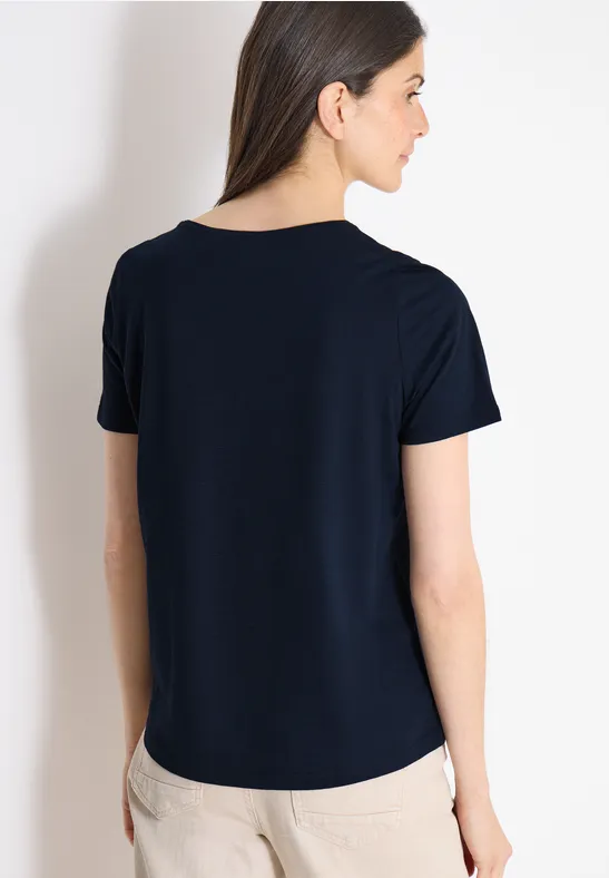 Rückansicht einer Frau in schlichtem dunkelblauen T-Shirt und beiger Hose.