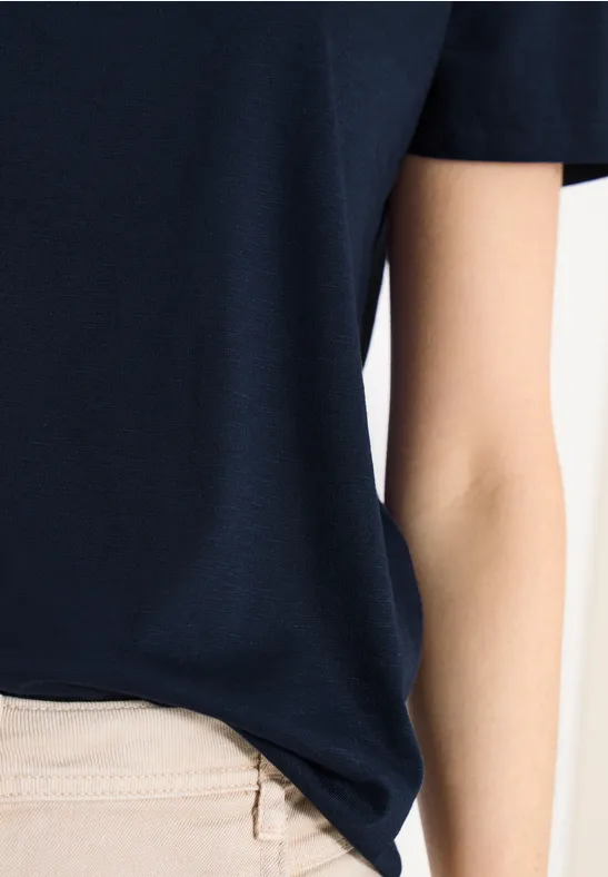 Person in dunkelblauem T-Shirt und beiger Hose, Nahaufnahme des Oberkörpers.