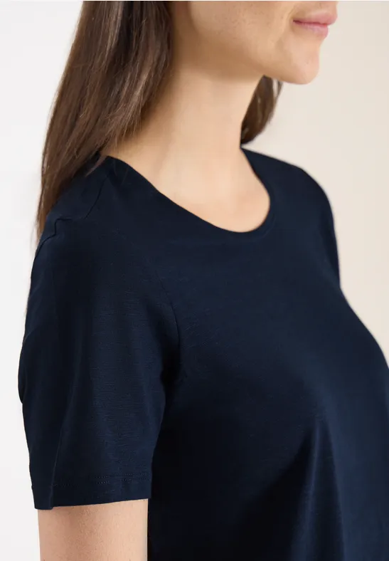 Nahaufnahme des Oberkörpers einer Frau im dunkelblauen Kurzarmshirt im Profil.