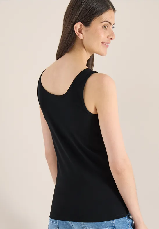 Eine Frau von hinten in einem schwarzen Tanktop, vor neutralem Hintergrund.