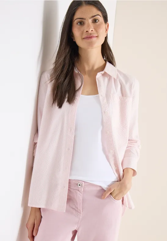 Frau in rosa Hemd, weißem Top und passenden rosa Hosen.